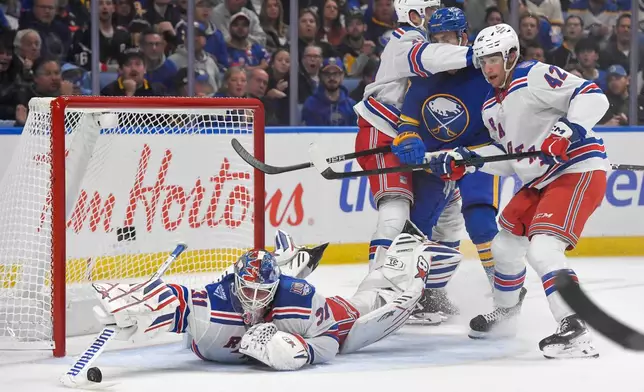 New York Rangers goalie Igor Shesterkin, left, reaches for a loose puck as defenseman Will Borgen, top left, and center Noah Laba, right, shield Buffalo Sabres left wing Jason Zucker during the second period of an NHL hockey game in Buffalo, N.Y., Thursday, Oct. 9, 2025. (AP Photo/Adrian Kraus)