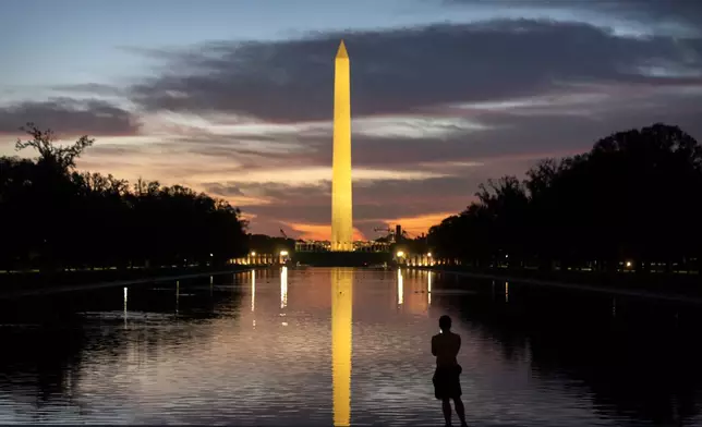 A visitor stands along the reflecting pool near the Washington Monument at dawn on Wednesday, Oct. 1, 2025, in Washington. (AP Photo/Mark Schiefelbein)
