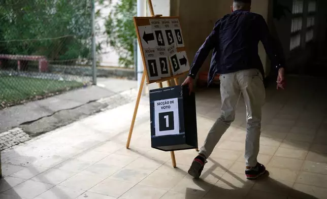 A worker picks up an empty ballot box at a polling station for Portugal's municipal elections in Lisbon, Sunday, Oct. 12, 2025. (AP Photo/Armando Franca)