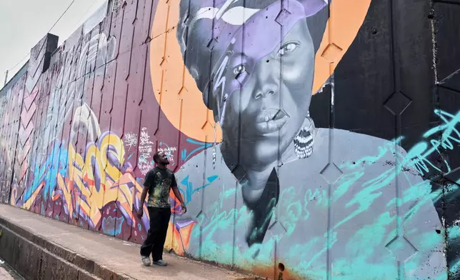 Graffiti artist Omar Diaw walks past one of his murals on a street wall in Conakry, Guinea, Saturday, Sep. 20, 2025. (AP Photo/Misper Apawu)