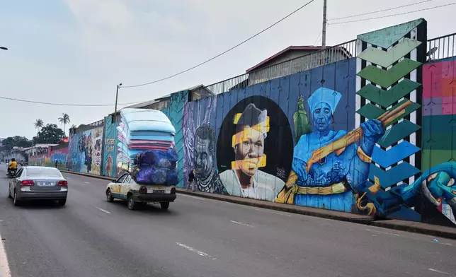 Cars drive past a long stretch of murals along a main road in Conakry, Guinea, Saturday, Sep. 20, 2025. (AP Photo/Misper Apawu)