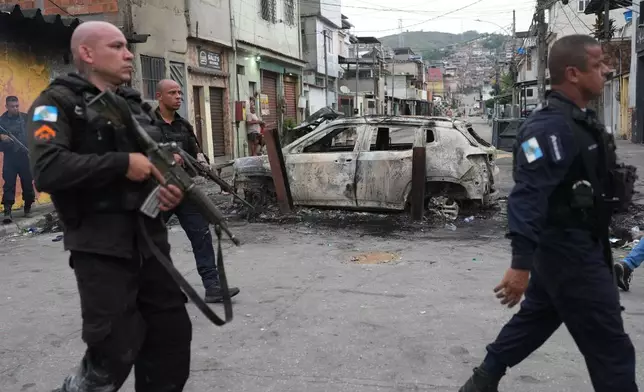 Police walk past a burned car used as a roadblock during a police operation against alleged drug traffickers in the Complexo do Alemao favela where the criminal organization "Comando Vermelho" operates in Rio de Janeiro, Tuesday, Oct. 28, 2025. (AP Photo/Silvia Izquierdo)