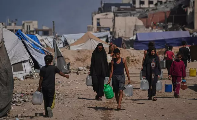Palestinians carry jerrycans and plastic bottles with water after collecting it at a camp for displaced people in Gaza City, Thursday Oct. 23, 2025. (AP Photo/Abdel Kareem Hana)