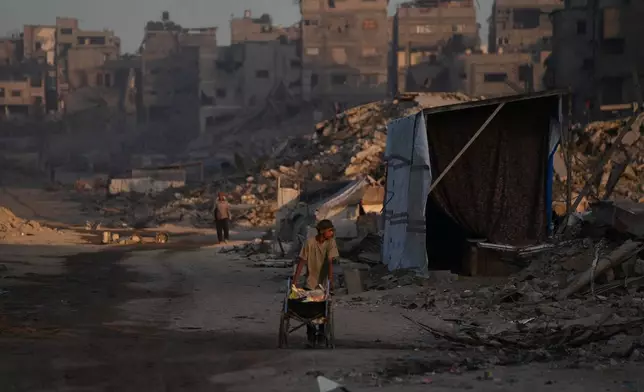 Palestinians walk trough the destruction caused by the Israeli air and ground offensive in Sheikh Radwan neighborhood in Gaza City, Wednesday, Oct. 22, 2025. (AP Photo/Abdel Kareem Hana)