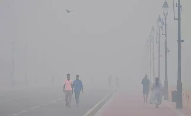 People walk in the morning near the India Gate monument amidst morning smog a day after Diwali festival in New Delhi, India, Tuesday, Oct. 21, 2025. (AP Photo/Manish Swarup)