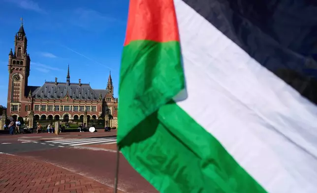 FILE -A Palestinian flag flies outside the International Court of Justice, rear, which opened hearings into a United Nations request for an advisory opinion on Israel's obligations to allow humanitarian assistance in Gaza and the West Bank, in The Hague, Netherlands, April 28, 2025. (AP Photo/Peter Dejong, File)
