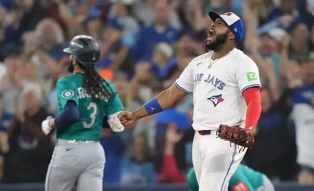 Toronto Blue Jays first base Vladimir Guerrero Jr. (27) celebrates an inning-ending double play as Seattle Mariners' J.P. Crawford (3) looks on during fourth inning MLB American League Championship Series game 6 baseball action in Toronto, Sunday, Oct. 19, 2025. (Nathan Denette/The Canadian Press via AP)