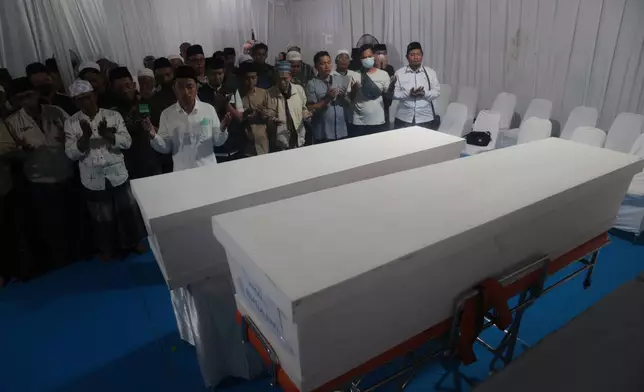 Men pray near the coffins containing the body of Nuruddin and Ahmad Rijalul Haq who are among the victims after a building under construction collapsed at an Islamic boarding school, during the handover of the bodies to the family members at the police hospital in Surabaya, East Java, Indonesia, Sunday, Oct. 5, 2025. (AP Photo/Trisnadi)