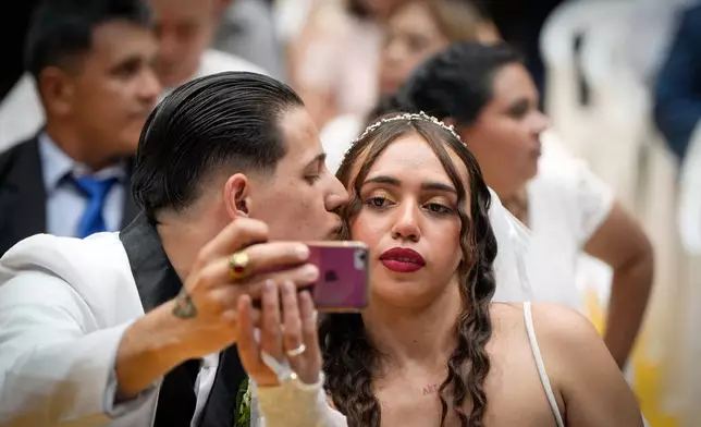 Jonathan Garay, left, and Fiorella Riveros take a selfie during a group wedding ceremony organized by the Civil Registry to legally formalize their unions in in Asuncion, Paraguay, Saturday, Oct. 4, 2025. (AP Photo/Jorge Saenz)