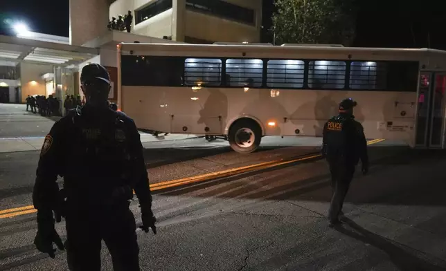 Law enforcement officers line the road outside a United States Immigration and Customs Enforcement (ICE) facility as a bus leaves with passengers on Tuesday, Oct. 21, 2025, in Portland, Ore. (AP Photo/Jenny Kane)