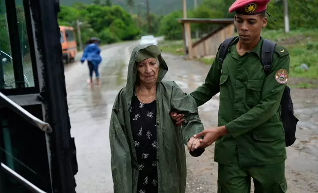A soldier helps a woman evacuate before the arrival of Hurricane Melissa in Canizo, a community in Santiago de Cuba, Tuesday, Oct. 28, 2025. (AP Photo/Ramon Espinosa)