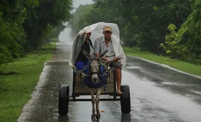 A couple rides under plastic on a donkey-pulled cart in the rain before the arrival of Hurricane Melissa in Canizo, a vilage in Santiago de Cuba, Tuesday, Oct. 28, 2025. (AP Photo/Ramón Espinosa)