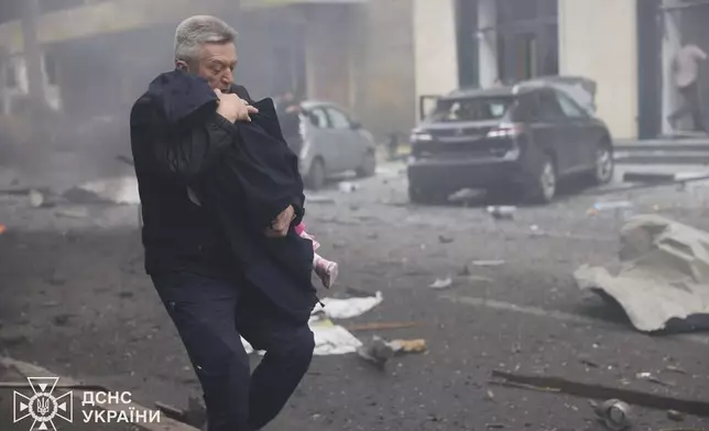 In this photo provided by the Ukrainian Emergency Service, a man evacuates a child after Russian drones hit a city kindergarten in Kharkiv, Ukraine, Wednesday, Oct. 22, 2025. (Ukrainian Emergency Service via AP)
