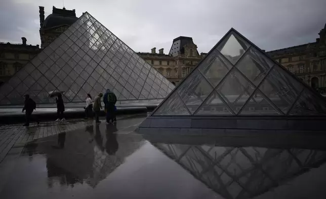 People tour the courtyard of Le Louvre museum in the rain Monday, Oct. 27, 2025 in Paris. (AP Photo/Christophe Ena)