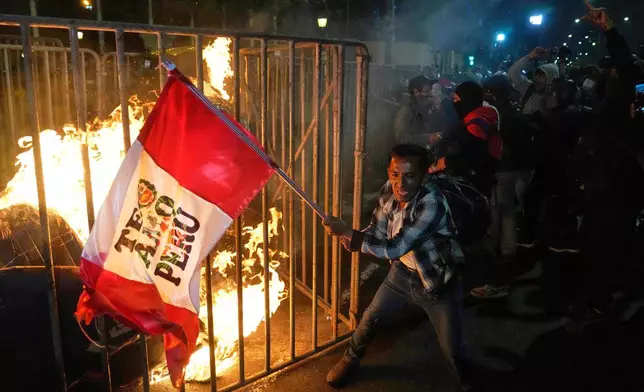 A demonstrator waves a Peruvian flag as a cardboard doll burns in front of Congress during a protest against new President Jose Jeri in Lima, Peru, Wednesday, Oct. 15, 2025. (AP Photo/Martin Mejia)