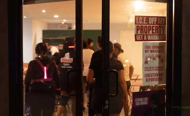 Members of the Huntington Park Run Club enter a pop-up coffee shop set up inside an art gallery in Huntington Park, Calif., Sept. 24, 2025, as signs on the door call for immigrant rights. (AP Photo/Jae C. Hong)