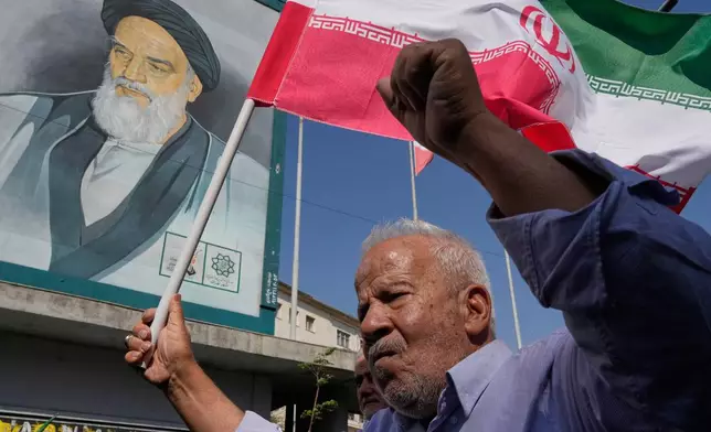 An Iranian worshipper holds his country's flag in front of a portrait of the late revolutionary founder Ayatollah Khomeini during an anti-Israeli rally after the Friday prayers at the Enqelab-e-Eslami (Islamic Revolution) street, in Tehran, Iran, Friday, Oct. 10, 2025. (AP Photo/Vahid Salemi)