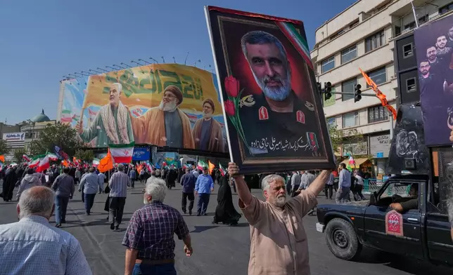 A man holds up a portrait of the late commander of Iran's Revolutionary Guard aerospace division Gen. Amir Ali Hajizadeh, who was killed in an Israeli strike in June, as a huge banner is seen at background showing the late commander of the Iran's Revolutionary Guard expeditionary Quds Force, Gen. Qassem Soleimani, left, who was killed in a U.S. drone attack in 2020, and two late Hezbollah leaders Hassan Nasrallah, center, and Hashem Safieddine, who were killed in Israeli airstrikes in 2024, during an anti-Israeli rally after the Friday prayers at the Enqelab-e-Eslami (Islamic Revolution) square, in Tehran, Iran, Friday, Oct. 10, 2025. (AP Photo/Vahid Salemi)