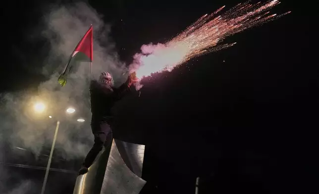 A protester, holding a Palestinian flag, launches fireworks toward the Israeli Embassy in Athens during a pro-Palestinian demonstration, Tuesday, Oct. 7, 2025, marking the two-year anniversary of Hamas' attack on Israel. (AP Photo/Petros Giannakouris)