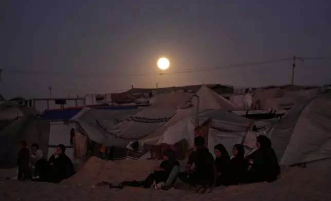 The moon rises behind a tent camp for displaced Palestinians along the Muwasi, an area that Israel has designated as a safe zone, in Khan Younis southern Gaza Strip Tuesday, Oct. 7, 2025. (AP Photo/Jehad Alshrafi)