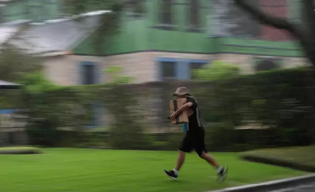 Venezuelan asylum seeker Luis, 30, runs through the rain as he delivers packages in Winter Park, Fla.,Tuesday, Aug. 19, 2025. Luis, who fled Venezuela after being an opposition political activist as a university student, was granted a longterm work permit, allowing him to support himself as an Amazon delivery driver as he goes through the legal asylum process. (AP Photo/Rebecca Blackwell)