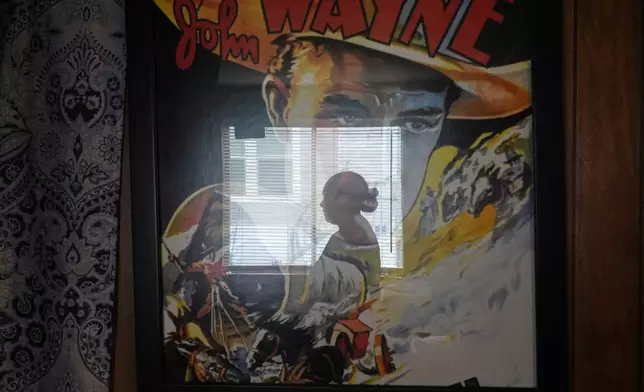 Paola Freites, who asked to be identified by her middle name and second last name to protect her family's safety, is reflected in a poster of John Wayne, who her teenaged son is a fan of, inside the two-bedroom mobile home where she lives with her husband and three children after fleeing persecution in their native Colombia, Thursday, Aug. 21, 2025, in Apopka, Fla. (AP Photo/Rebecca Blackwell)