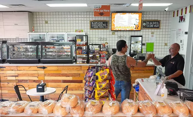 Dario Romero, right, co-owner of Venezuelan restaurant TeqaBite, greets a customer, Thursday, Aug. 21, 2025, in Kissimmee, Fla. Despite a big increase in the local Venezuelan population in the last several years, Romero says the restaurant has recently struggled to fill job openings and business is down. An immigration crackdown under President Donald Trump has led to some migrants losing their legal status and work permits, while many others still in legal processes are too fearful to venture out of the house except to go to and from work. (AP Photo/Rebecca Blackwell)