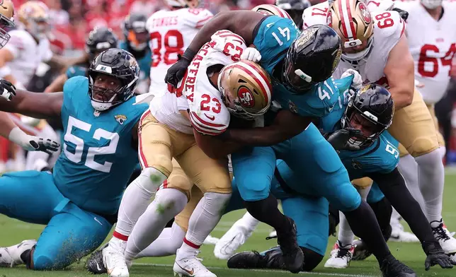 San Francisco 49ers running back Christian McCaffrey (23) is stopped while running against Jacksonville Jaguars defensive end Josh Hines-Allen (41), DaVon Hamilton and defensive tackle Arik Armstead (91) during the first half of an NFL football game in Santa Clara, Calif., Sunday, Sept. 28, 2025. (AP Photo/Kelley L. Cox)