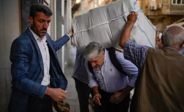 Porters place a load on a co-worker's back in the Eminonu commercial area of Istanbul, Turkey, Wednesday, Sept. 24, 2025. (AP Photo/Emrah Gurel)