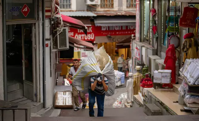 A porter carries a load on his back up the stairs in the Eminonu commercial area of Istanbul, Turkey, Thursday, Oct. 2, 2025. (AP Photo/Emrah Gurel)