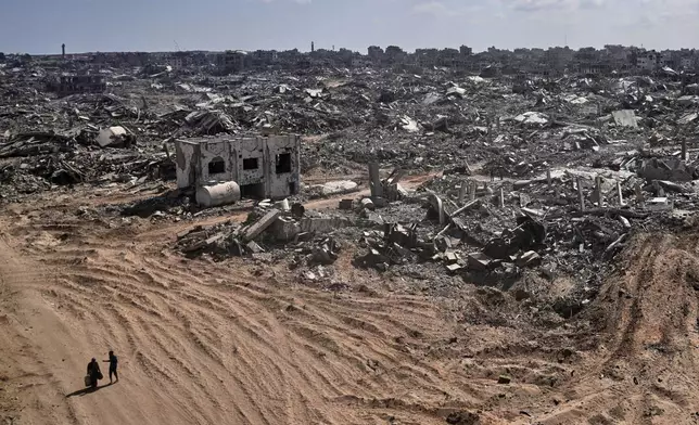 Two displaced Palestinians walk past destroyed buildings in the heavily damaged Sheikh Radwan neighborhood in Gaza City, Saturday, Oct. 11, 2025, after Israel and Hamas agreed to a pause in their war and the release of the remaining hostages. (AP Photo/Abdel Kareem Hana)