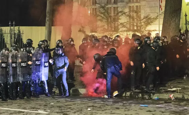 Police extinguish a flare thrown at them during an opposition rally in the city center of Tbilisi, Georgia, on Saturday, Oct. 4, 2025, boycotting the municipal elections and calling for the release of political opponents. (AP Photo/Zurab Tsertsvadze)