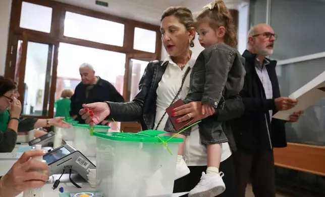 A woman with a girl lines up to get her ballot at a polling station during the municipal elections in Tbilisi, Georgia, on Saturday, Oct. 4, 2025. (AP Photo/Zurab Tsertsvadze)