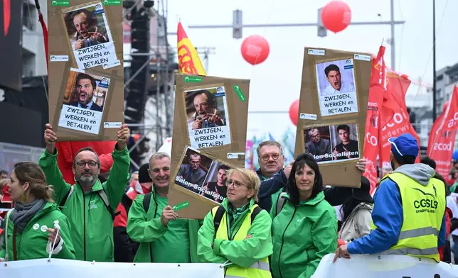 Demonstrators hold signs with photos of Belgian politicians which reads 'keep quiet, work and pay', during a general strike in Brussels, Tuesday, Oct. 14, 2025. (AP Photo/Harry Nakos)