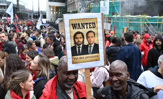 Two men hold a sign with a photo of Belgium's Prime Minister Bart De Wever, which reads 'Pension Theft', during a demonstration and general strike in Brussels, Tuesday, Oct. 14, 2025. (AP Photo/Harry Nakos)