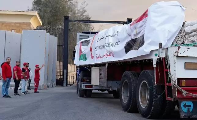Egyptian Red Crecent members monitor trucks carrying humanitarian aids as they enter the Rafah crossing between Egypt and the Gaza Strip, following an agreement between Israel and Hamas on a ceasefire, Sunday, Oct. 12, 2025. (AP Photo/Mohamed Arafat)