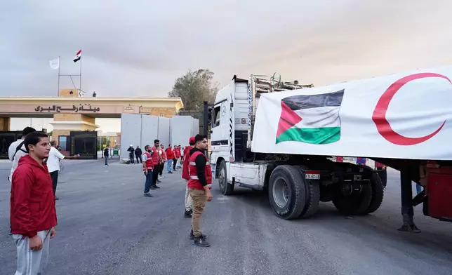 Egyptian Red Crecent members monitor trucks carrying humanitarian aid as they enter the Rafah crossing between Egypt and the Gaza Strip, following an agreement between Israel and Hamas on a ceasefire, Sunday, Oct. 12, 2025. (AP Photo/Mohamed Arafat)