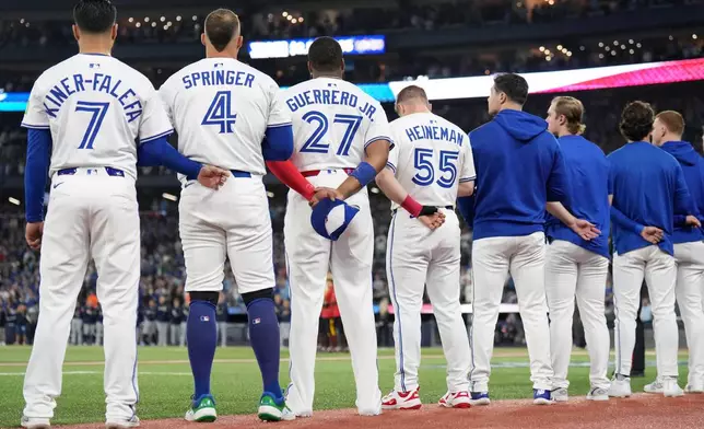 Toronto Blue Jays' Isiah Kiner-Falefa (7), George Springer (4), Vladimir Guerrero Jr. (27), Tyler Heineman (55) and members of the bullpen line up for the singing of the national anthems ahead of Game 7 of baseball's American League Championship Series against the Seattle Mariners in Toronto, Monday, Oct. 20, 2025. (Nathan Denette/The Canadian Press via AP)
