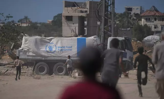 Palestinians rush toward trucks carrying aid from the World Food Programme (WFP) as they drive through Deir al-Balah in central Gaza, Wednesday, Oct. 15, 2025. (AP Photo/Abdel Kareem Hana)