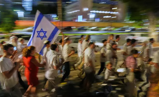 Jewish revelers dance and hold up the Torah as they celebrate the holiday of Simchat Torah next to the plaza known as hostages square, in Tel Aviv, Israel, Tuesday, Oct. 14, 2025. (AP Photo/Francisco Seco)