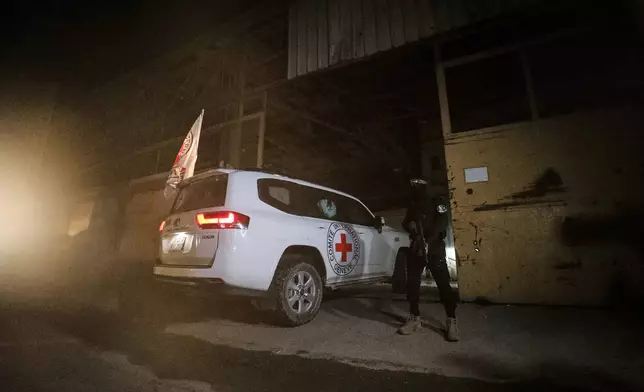 A gunman wearing the uniform of the al-Qassam Brigades, the military wing of Hamas, stands guard as Red Cross vehicles enter a warehouse allegedly to collect coffins containing the bodies of four deceased hostages, in Gaza City, Tuesday, Oct. 14, 2025. (AP Photo/Yousef Al Zanoun)