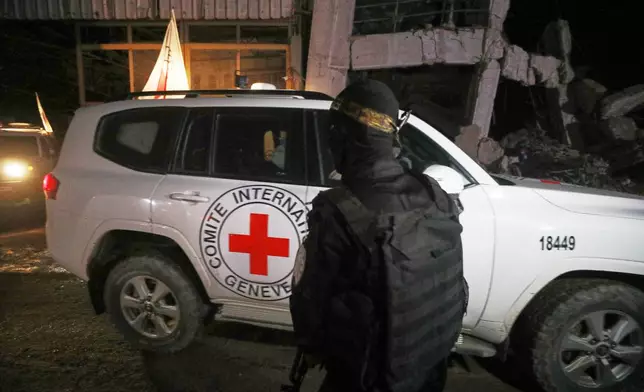 A gunman wearing the uniform of the al-Qassam Brigades, the military wing of Hamas, stands guard as Red Cross vehicles allegedly transporting coffins containing the bodies of four deceased hostages leave a warehouse for Israel, in Gaza City, Tuesday, Oct. 14, 2025. (AP Photo/Yousef Al Zanoun)