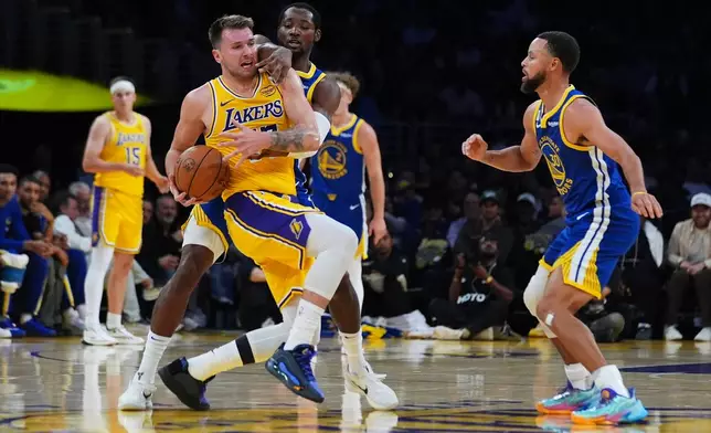 Los Angeles Lakers' Luka Dončić, left, is defended by Golden State Warriors guard Jonathan Kuminga during the first half of an NBA basketball game Tuesday, Oct. 21, 2025, in Los Angeles. (AP Photo/Ethan Swope)