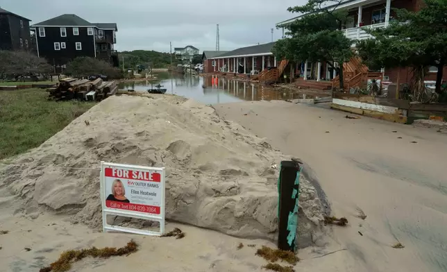 A "For Sale" sign its on a flooded road after a storm, Monday, Oct. 13, 2025, in Buxton, N.C. (AP Photo/Allison Joyce)