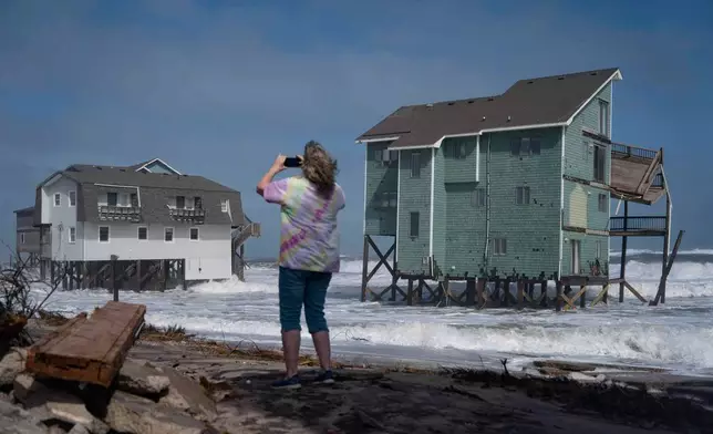 A person stands and takes photos of houses at risk of collapse in the midst of a storm, Sunday, Oct. 12, 2025, in Buxton, N.C. (AP Photo/Allison Joyce)