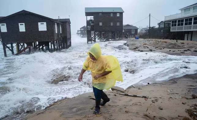 A man walks past houses at risk of collapse in the midst of a storm, Sunday, Oct. 12, 2025, in Buxton, N.C. (AP Photo/Allison Joyce)