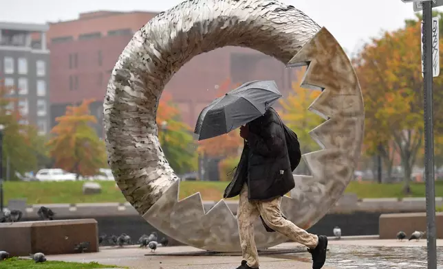 C. Johnson, of Providence, R.I., carries an umbrella, Monday, Oct. 13, 2025, while walking along a rain-soaked walkway near a sculpture, in Providence, R.I. (Photo/Steven Senne)
