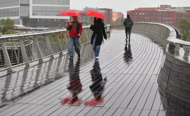 Stanislav Valchev, of Providence, R.I., left, and Dari Dimitrova, of Lewisburg, Penn., center, carry umbrellas while walking on a rain-soaked bridge, Monday, Oct. 13, 2025, in Providence. (Photo/Steven Senne)