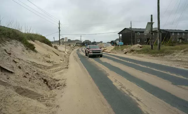 A car drives over sand on Highway 12 after a storm, Monday, Oct. 13, 2025, in Buxton, N.C. (AP Photo/Allison Joyce)