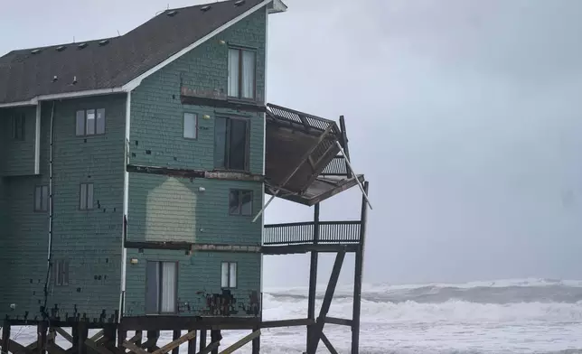 A balcony hangs off a home at risk of collapse in the midst of a storm, Sunday, Oct. 12, 2025, in Buxton, N.C. (AP Photo/Allison Joyce)